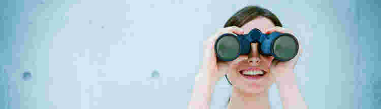 Woman looking through binoculars with friendly smile